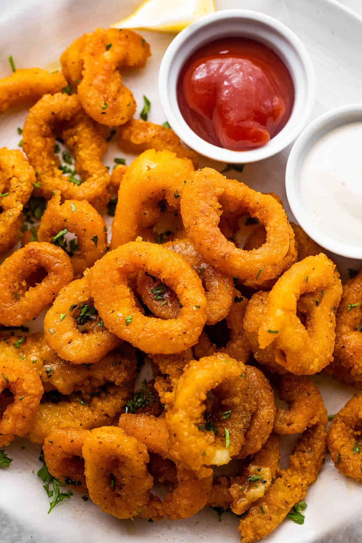 plate with a stack of air fried calamari and a small bowl of ketchup served on the side