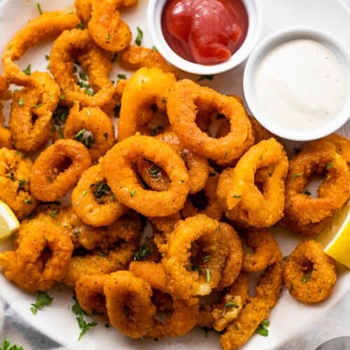 plate with a stack of air fried calamari and a small bowl of ketchup served on the side