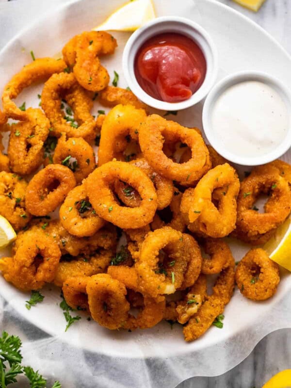 plate with a stack of air fried calamari and a small bowl of ketchup served on the side