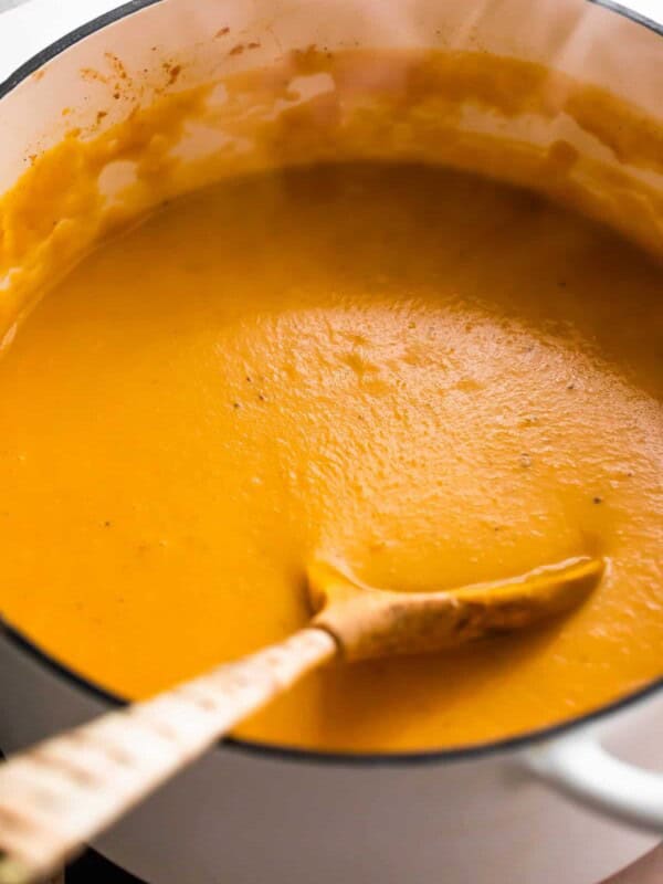 Curried Butternut Squash Soup in a white Dutch oven with a wooden spoon inside the pot