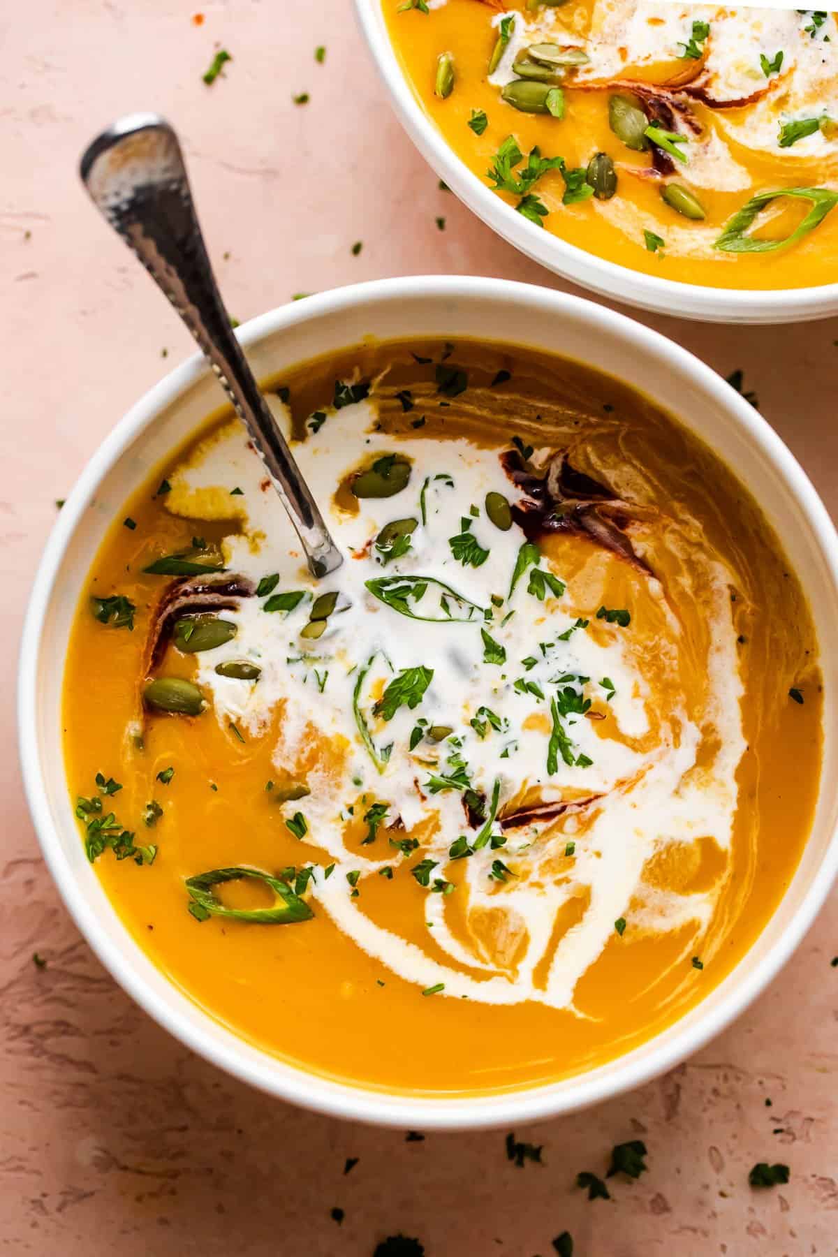overhead shot of a bowl of butternut squash soup garnished with cream, pumpkin seeds, and greens