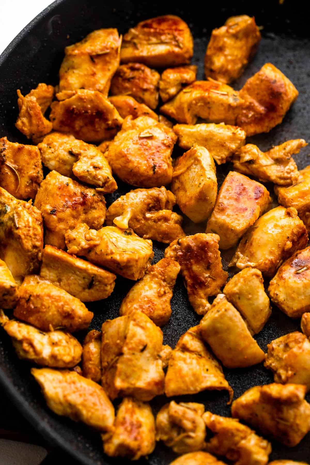 cooking chunks of chicken breast pieces in a black skillet