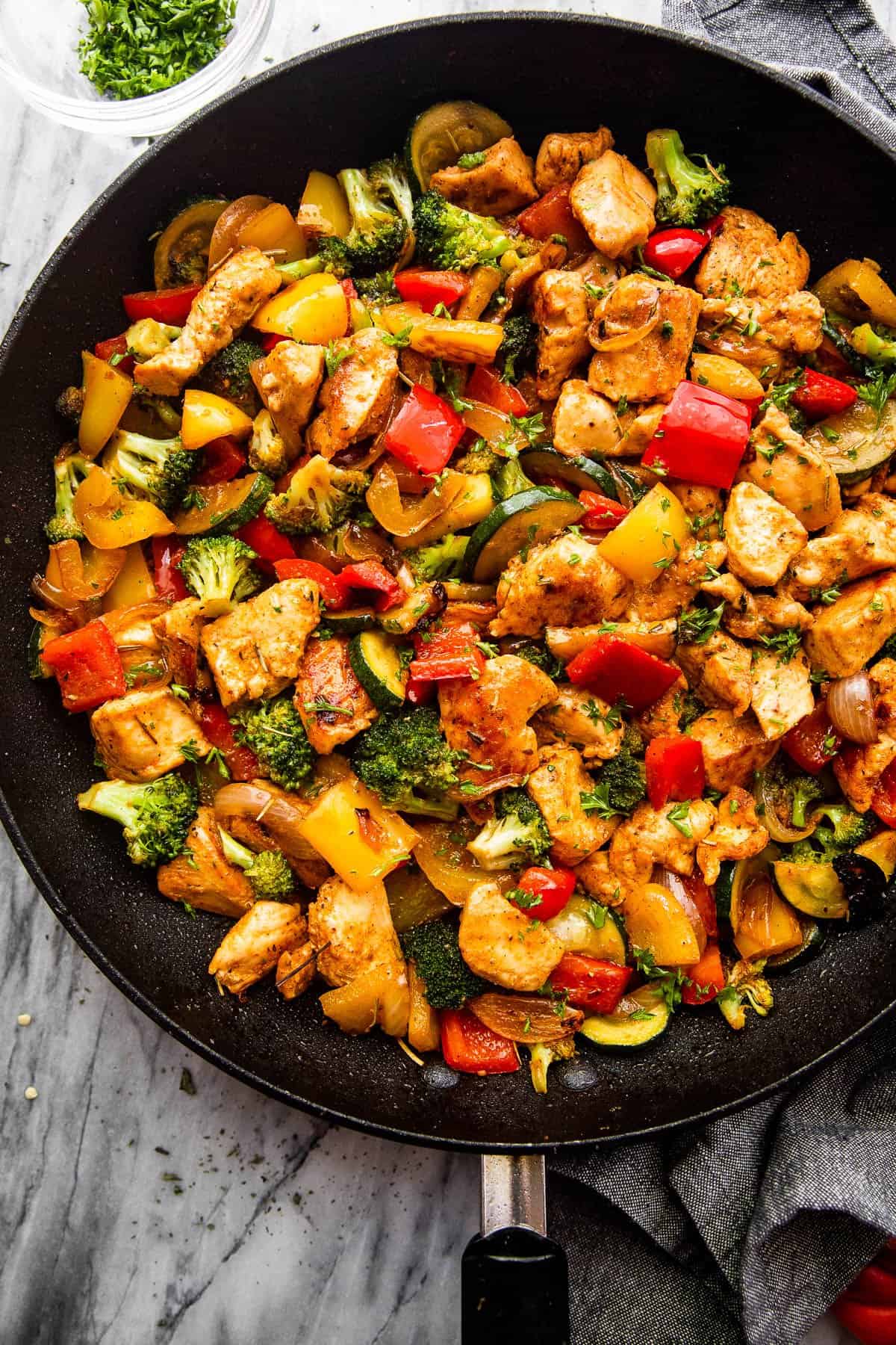 overhead shot of cut up chicken breast cooked in a skillet with zucchini, broccoli, and bell peppers