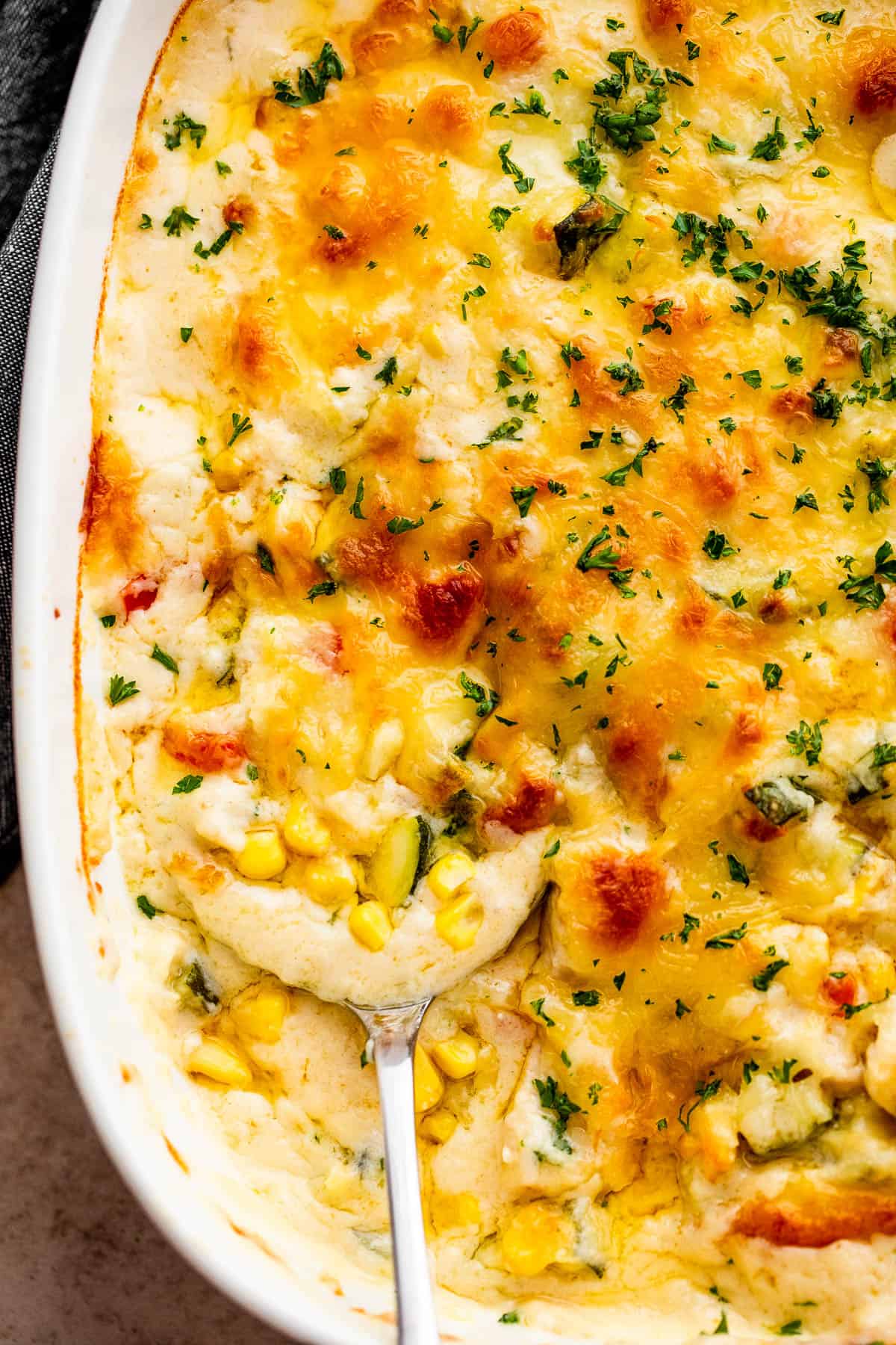 A serving spoon scooping up chicken zucchini casserole from a baking dish.