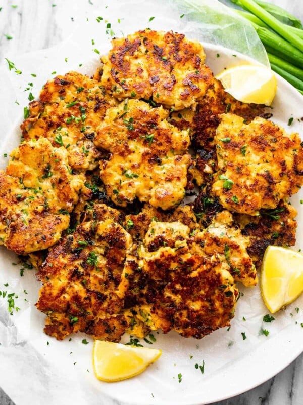 zucchini chicken fritters served on a plate with lemon wedges and green onions to the side.