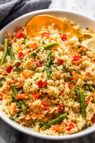 couscous served in a white bowl and garnished with asparagus pieces, shredded carrots, raisins, and diced red bell pepper