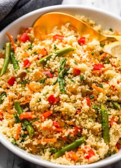 couscous served in a white bowl and garnished with asparagus pieces, shredded carrots, raisins, and diced red bell pepper