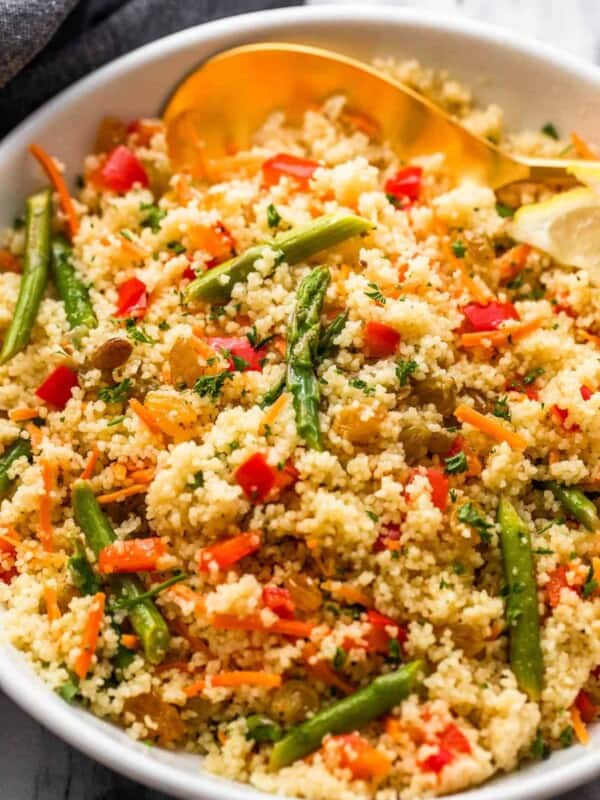 couscous served in a white bowl and garnished with asparagus pieces, shredded carrots, raisins, and diced red bell pepper