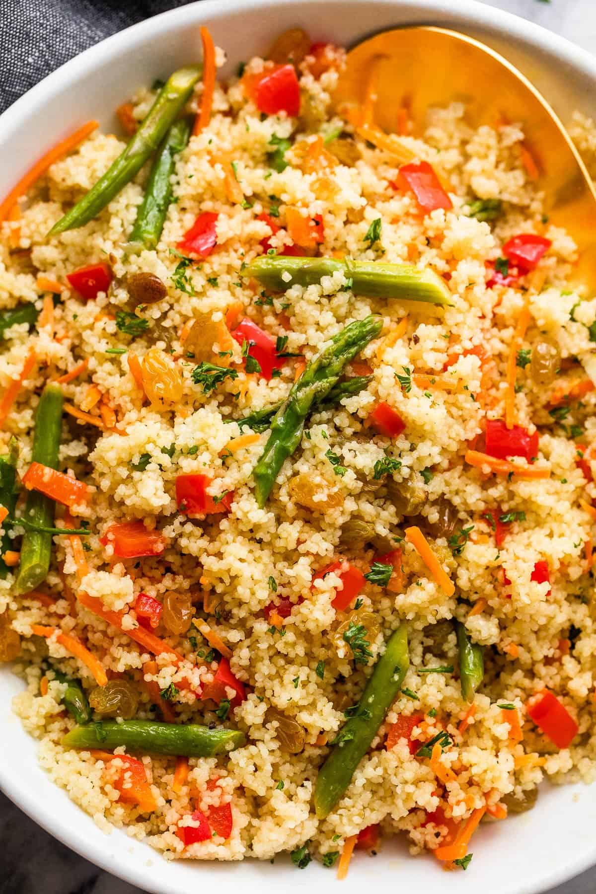 couscous served in a white bowl and garnished with asparagus pieces, shredded carrots, raisins, and diced red bell pepper