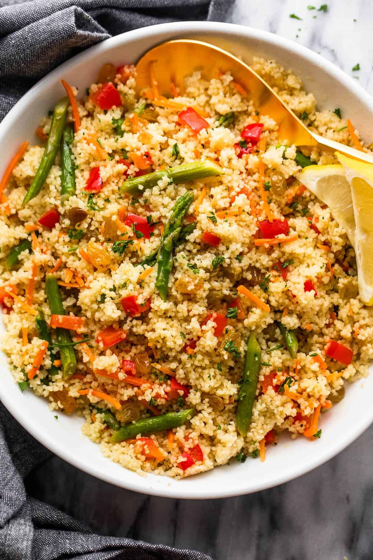 couscous served in a white bowl and garnished with asparagus pieces, shredded carrots, raisins, and diced red bell pepper