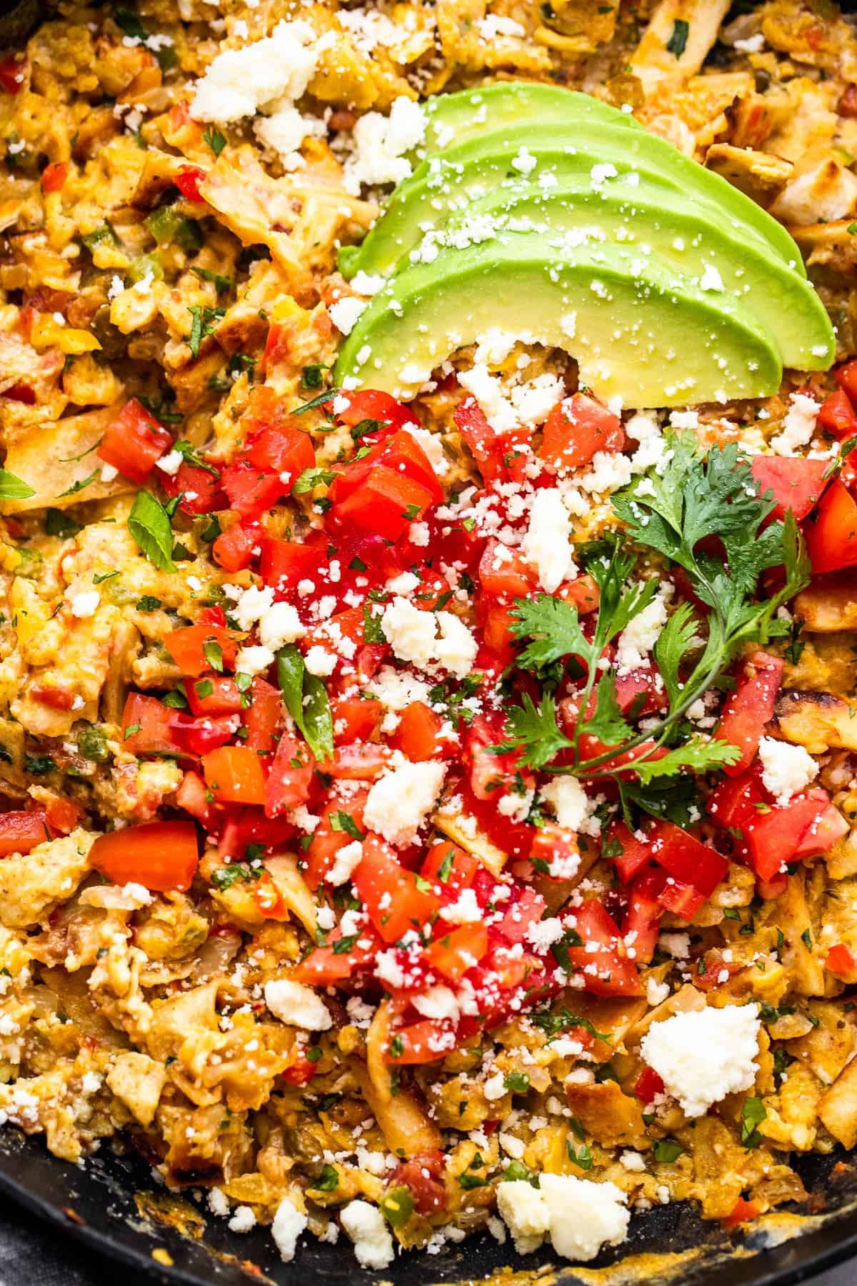 skillet with scrambled eggs, sliced avocados, diced tomatoes, and crumbled cotija cheese