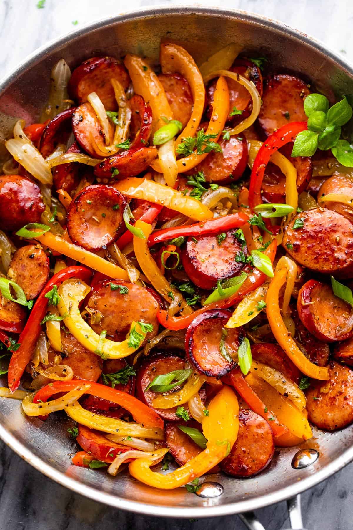 Overhead close-up image of cooked sliced andouille sausage and bell peppers in a skillet. 