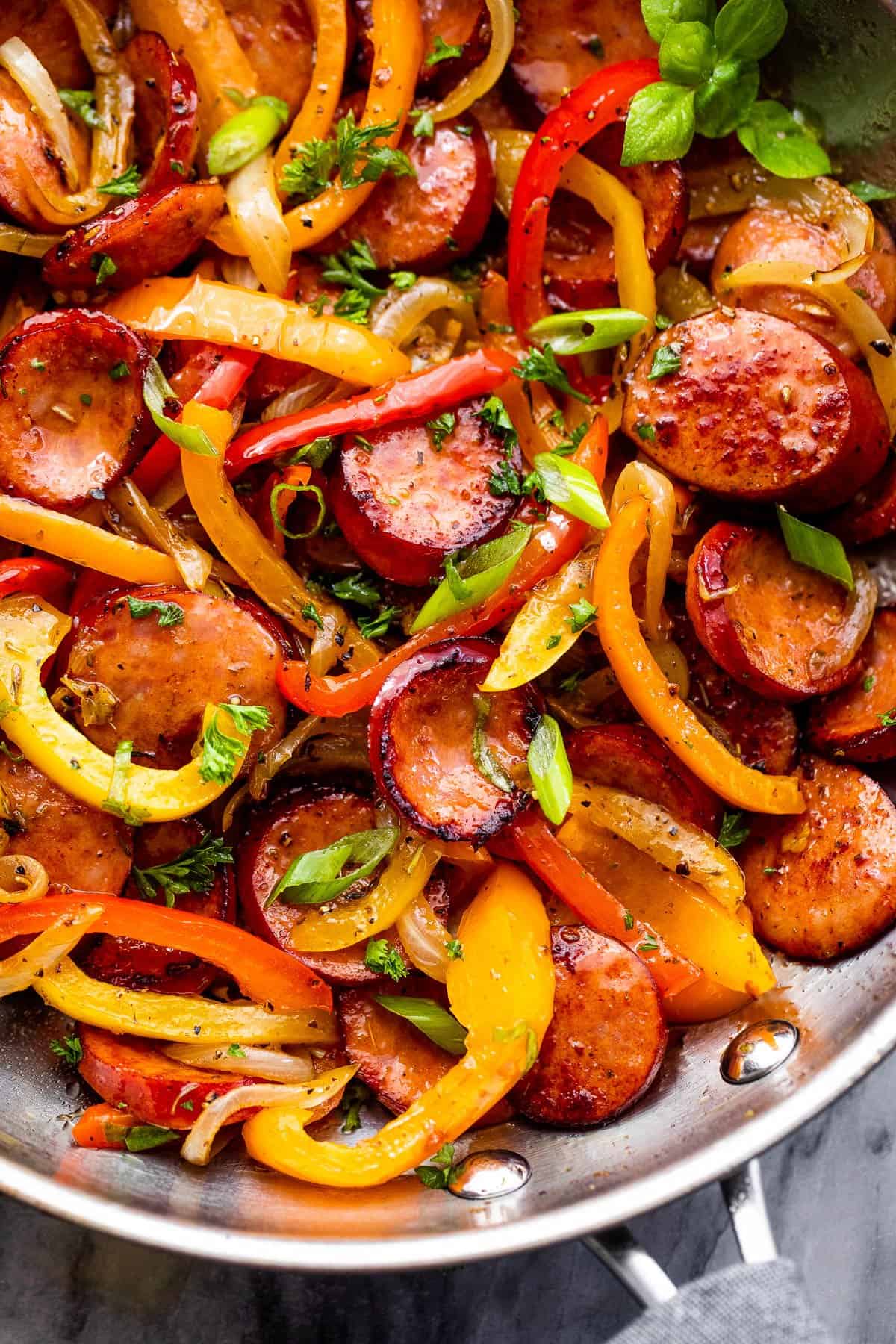 Close-up photo of sliced bell peppers, andouille sausage slices, and onions in a skillet.