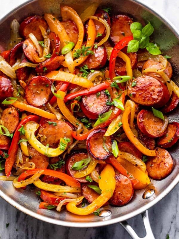 stainless steel skillet with cooked sliced peppers, sausages, and onions