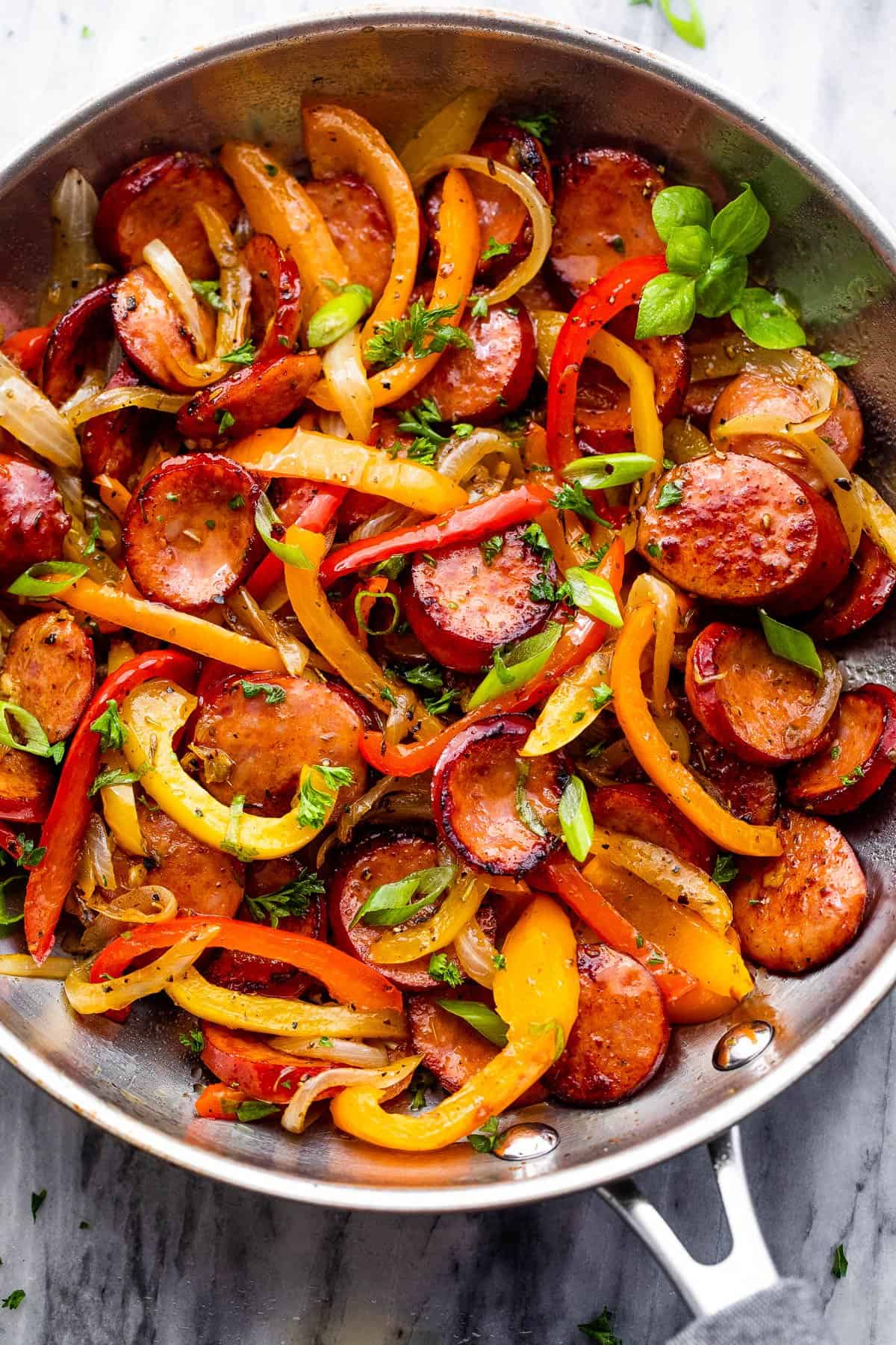 stainless steel skillet with cooked sliced peppers, sausages, and onions