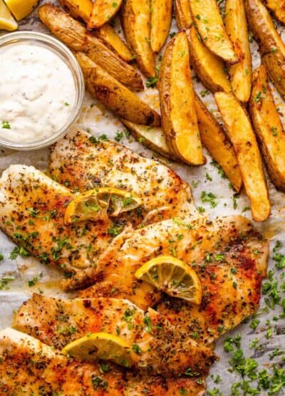 three fish fillets served with potato wedges and tartar sauce.