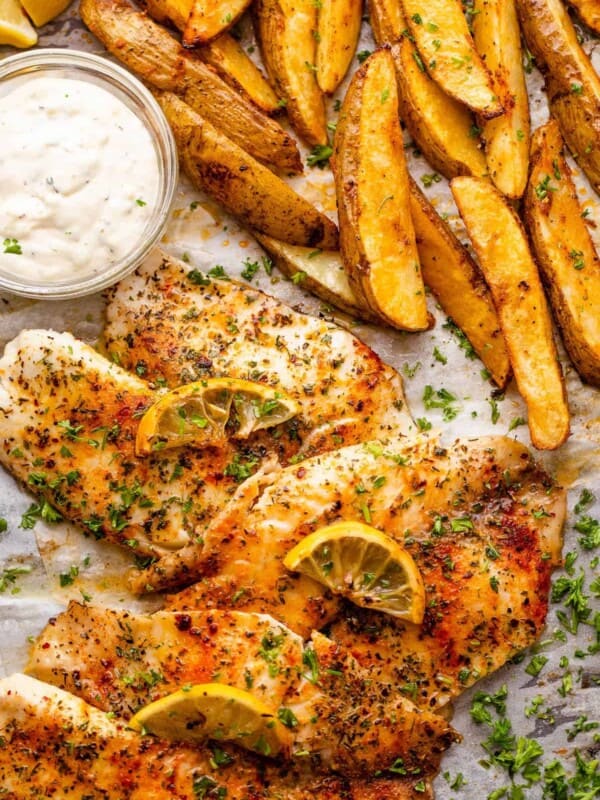 three fish fillets served with potato wedges and tartar sauce.