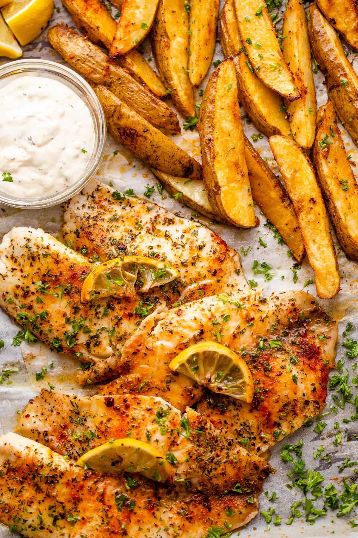 three fish fillets served with potato wedges and tartar sauce.