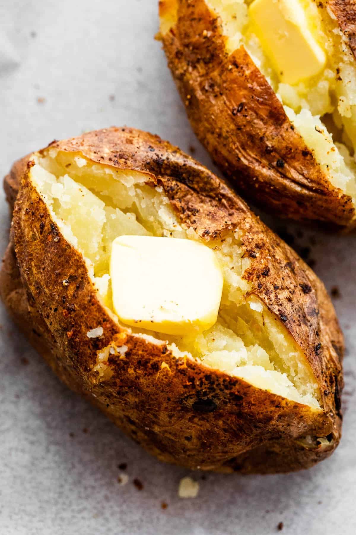 air fryer baked potato cut open on top and a pat of butter served over it.