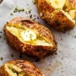 three air fryer baked potatoes cut open on top and a pat of butter served over it.