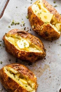 three air fryer baked potatoes cut open on top and a pat of butter served over it.