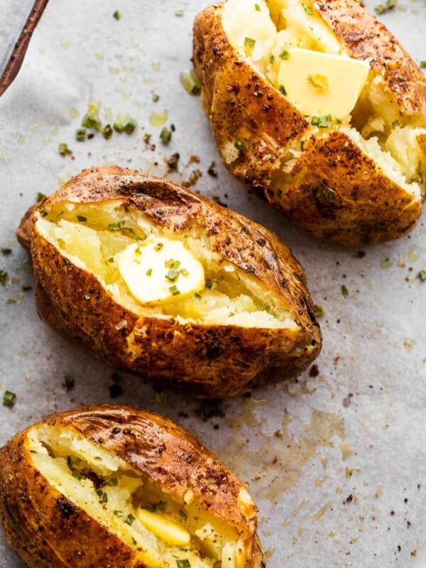 three air fryer baked potatoes cut open on top and a pat of butter served over it.