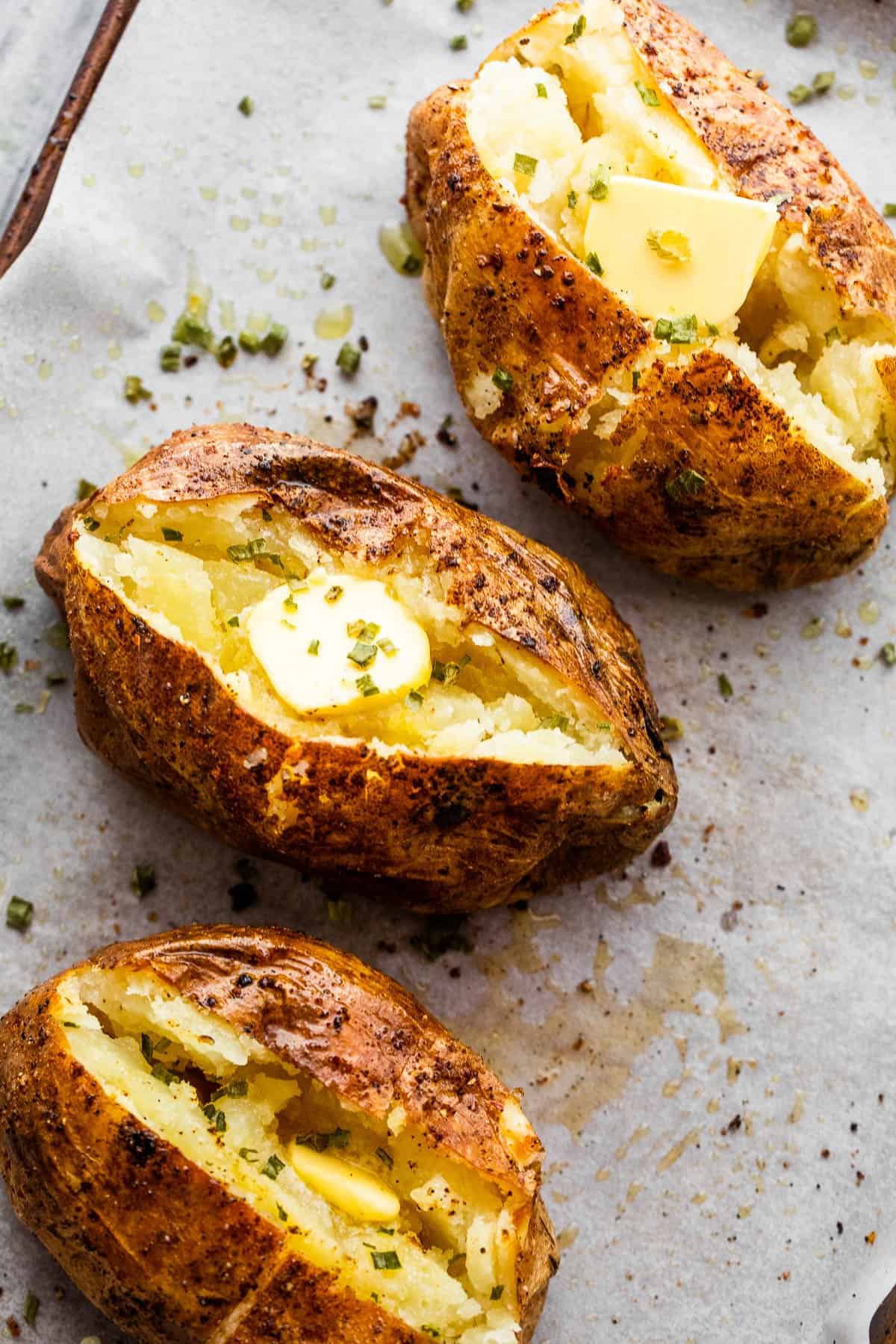 Three air fryer baked potatoes cut open on top and a pat of butter served over it.