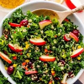 Crunchy Kale Quinoa Salad in a white bowl with a wooden spoon inside the bowl.