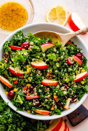 Crunchy Kale Quinoa Salad in a white bowl with a wooden spoon inside the bowl.