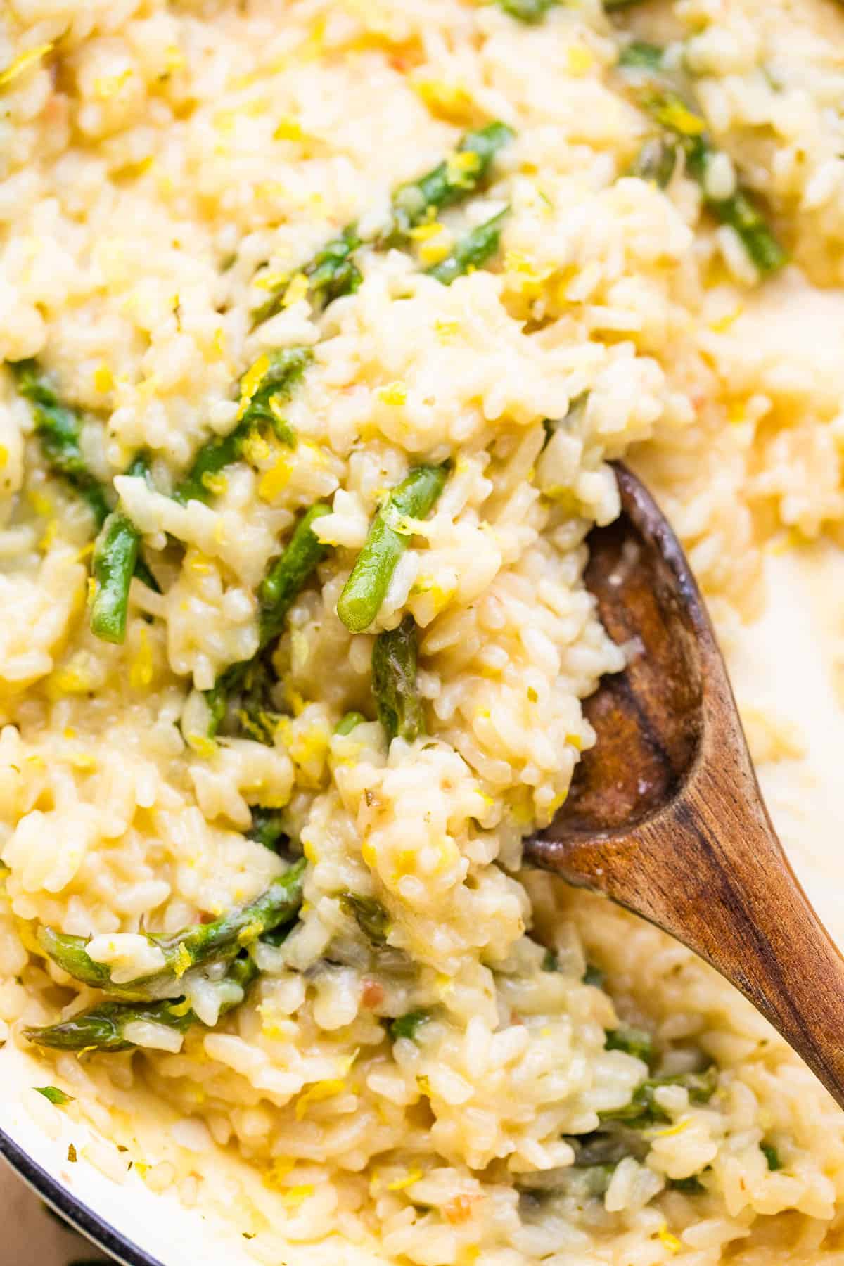 Close-up of a wooden spoon stirring through cooked risotto with asparagus.