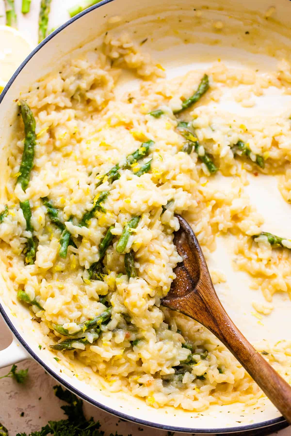 Wooden spoon stirring through cooked risotto with asparagus.