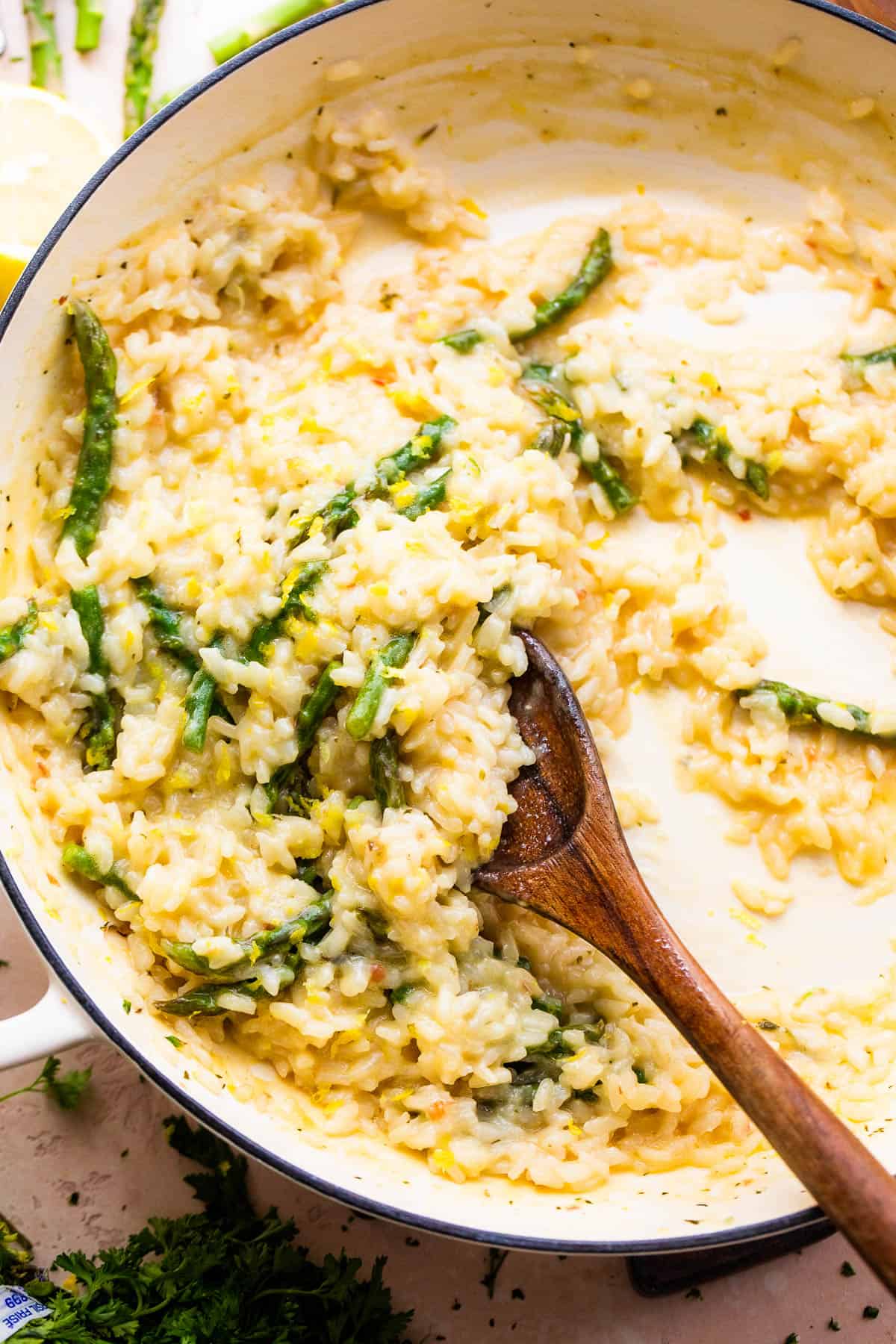 Wooden spoon stirring through cooked risotto with asparagus.