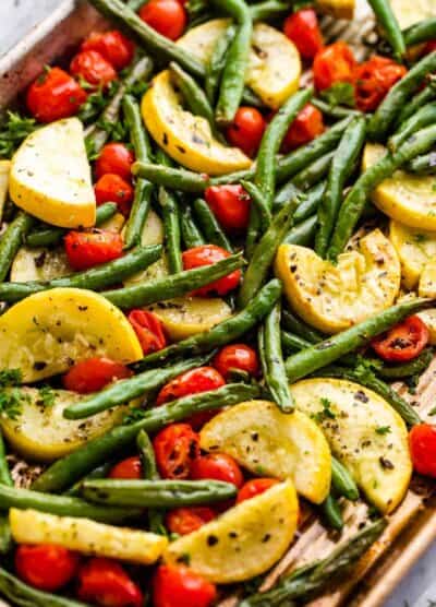 halved cherry tomatoes, halved yellow squash, and whole green beans on a sheet pan