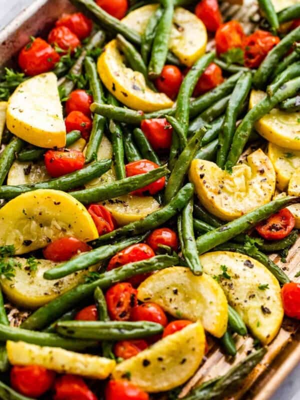 halved cherry tomatoes, halved yellow squash, and whole green beans on a sheet pan