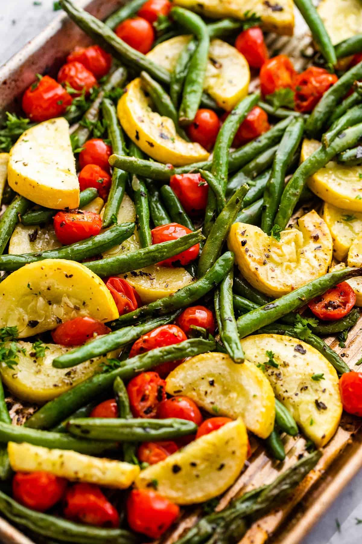 halved cherry tomatoes, halved yellow squash, and whole green beans on a sheet pan