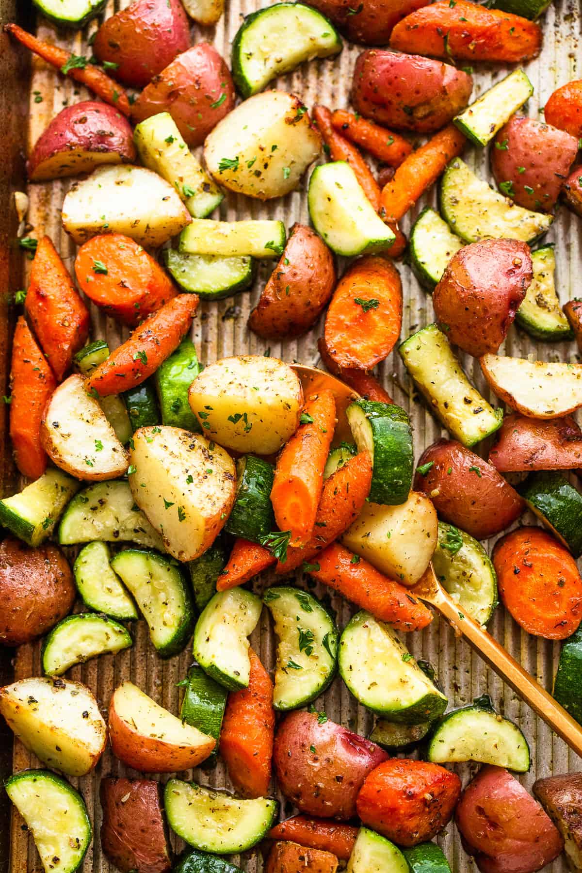 mixing through a pan with roasted potatoes, carrots, and zucchini