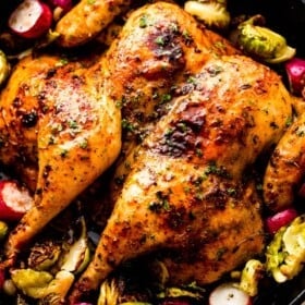 overhead photo of roasted spatchcock chicken, brussel sprouts, and radishes in a black cast iron skillet