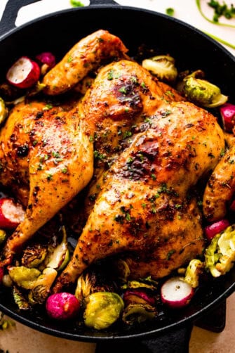 overhead photo of roasted spatchcock chicken, brussel sprouts, and radishes in a black cast iron skillet