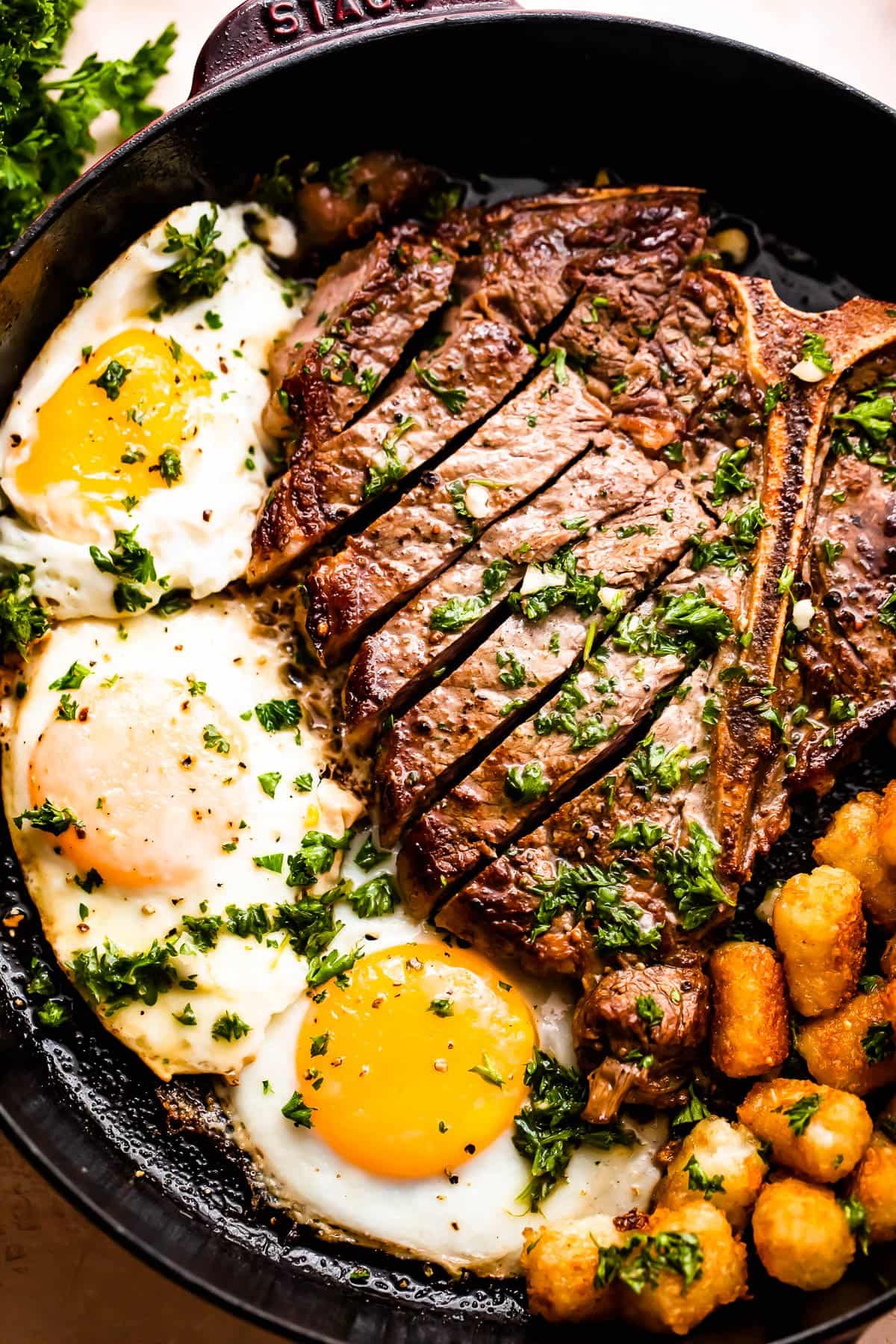 close up shot of a skillet with t-bone steak cut in slices and served next to three eggs cooked over easy .