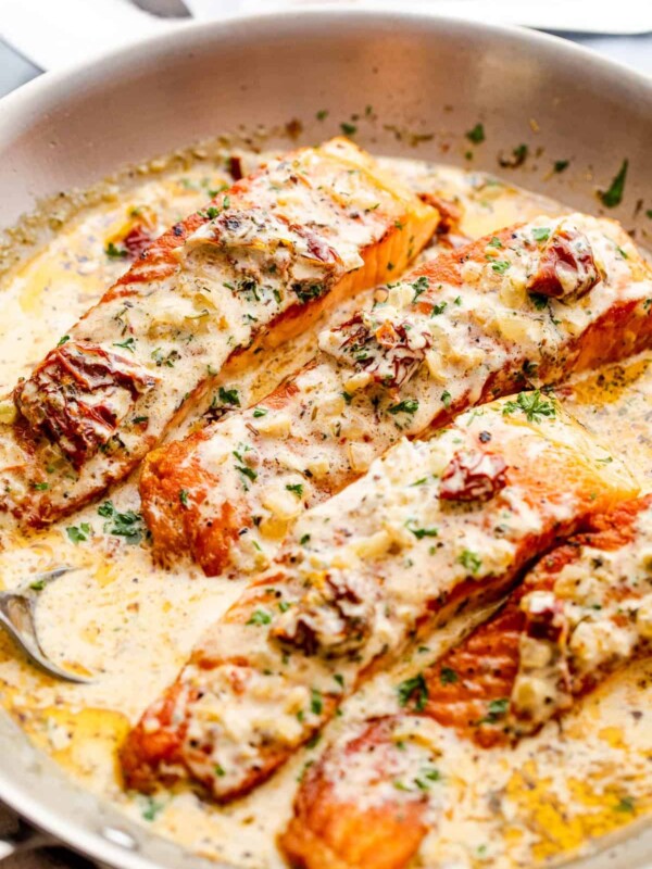 four salmon fillets in a skillet with cream sauce