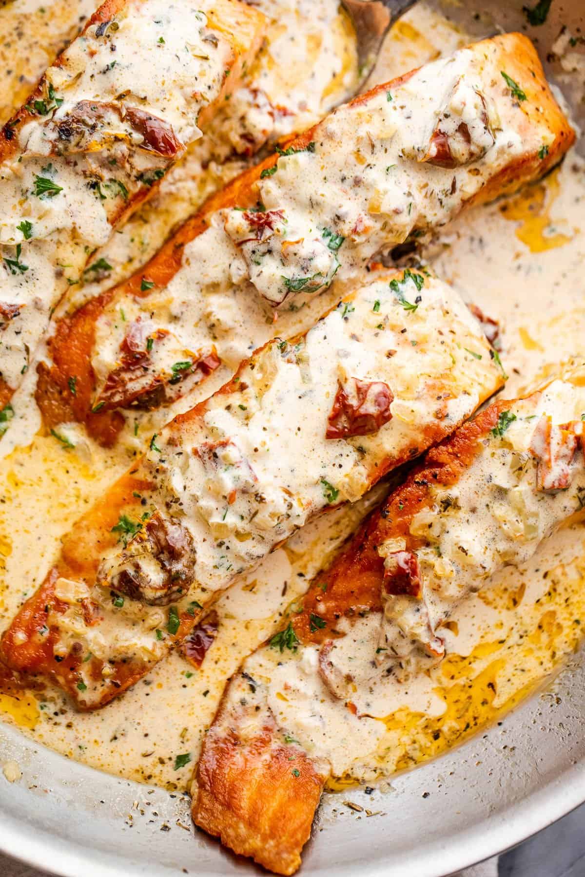 overhead shot of four salmon fillets in a skillet with cream sauce