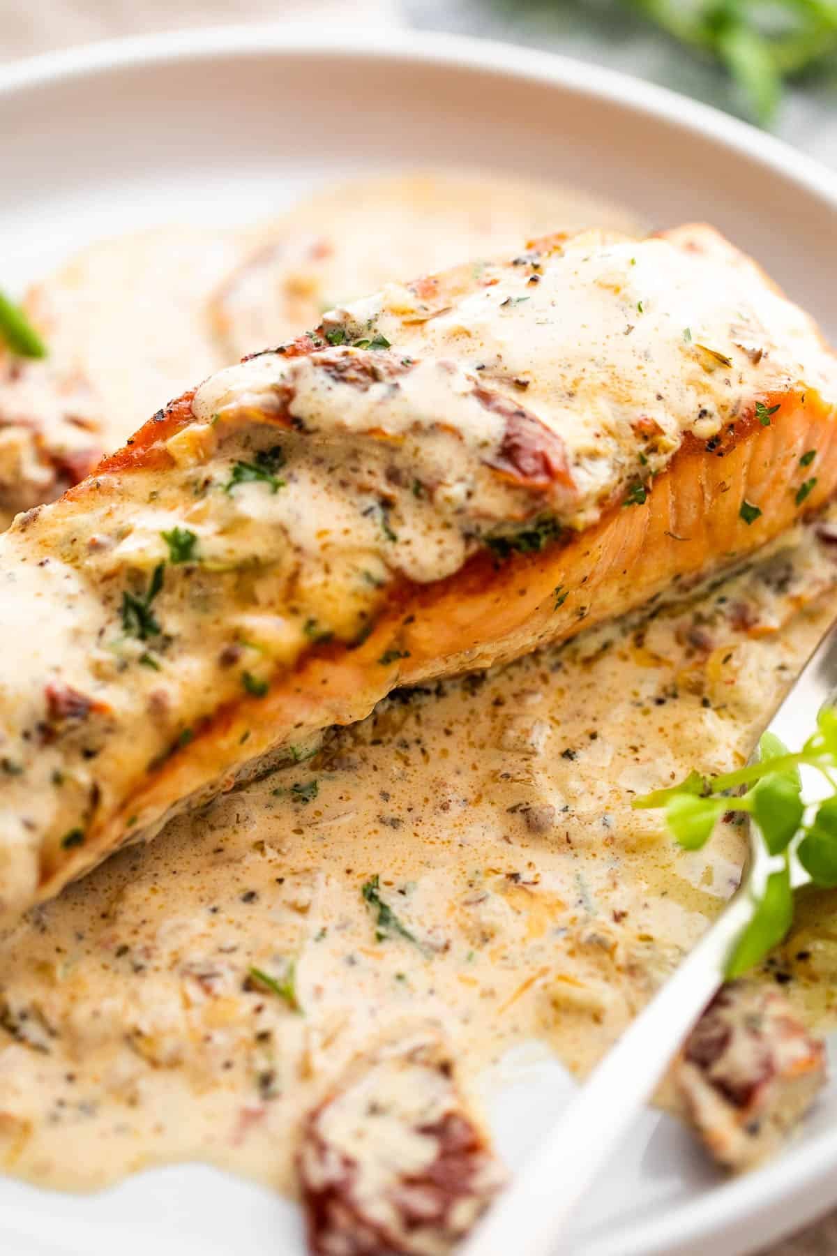 Cooked salmon fillet topped with cream sauce and served on a plate.