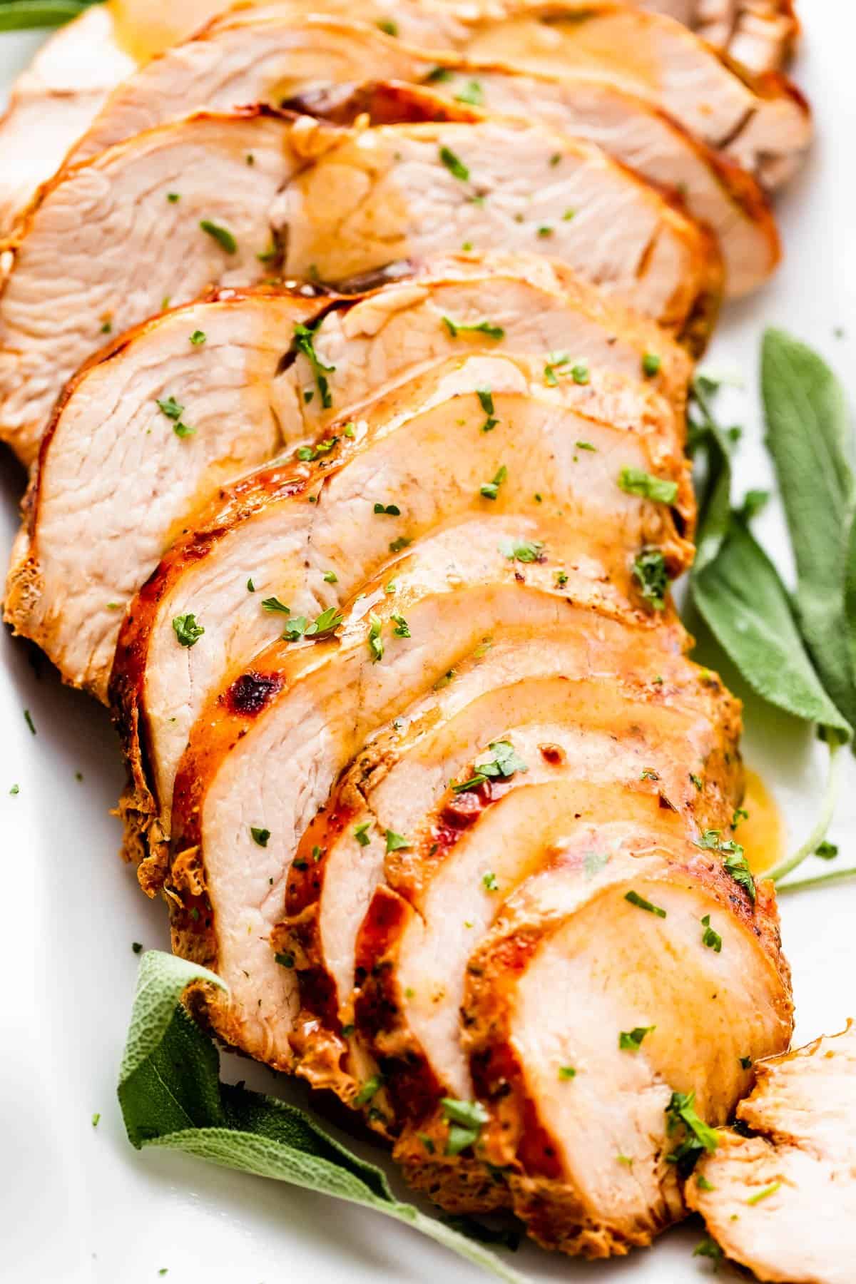 sliced air fryer turkey breast drizzled with gravy and arranged on a white platter with sage leaves placed on the sides of the turkey breast