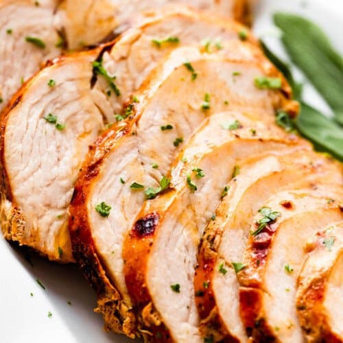 sliced air fryer turkey breast drizzled with gravy and arranged on a white platter with sage leaves placed on the sides of the turkey breast