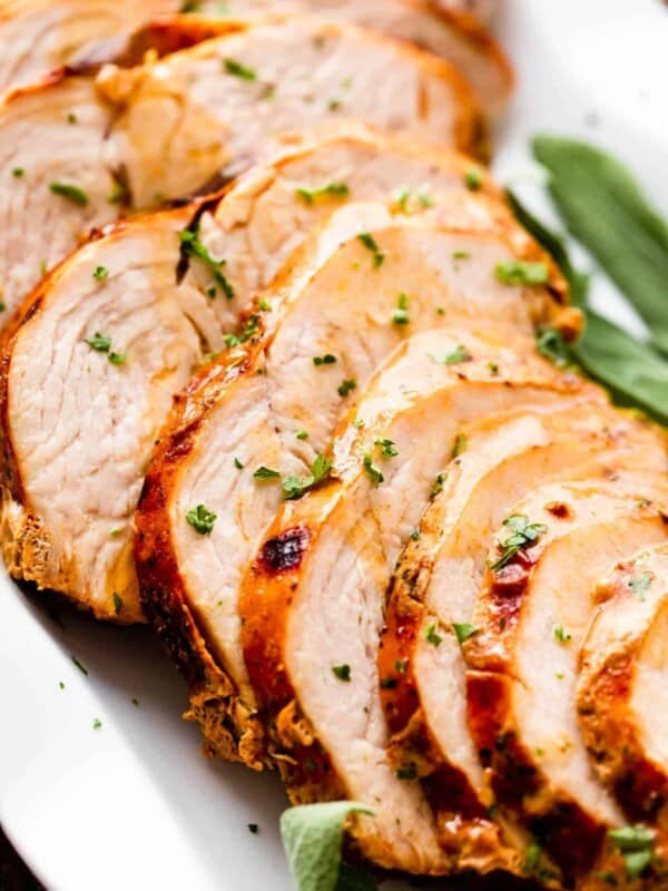 sliced air fryer turkey breast drizzled with gravy and arranged on a white platter with sage leaves placed on the sides of the turkey breast