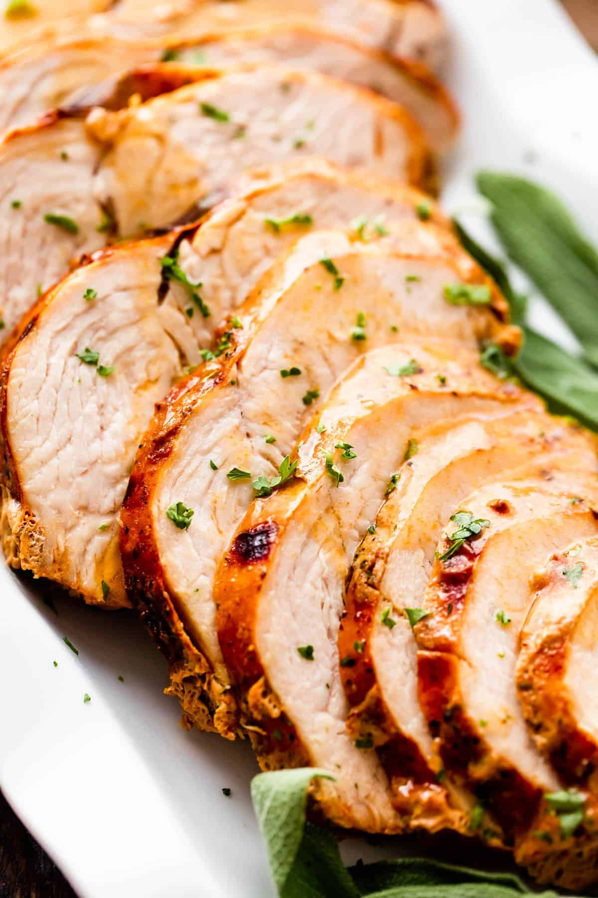 sliced air fryer turkey breast drizzled with gravy and arranged on a white platter with sage leaves placed on the sides of the turkey breast