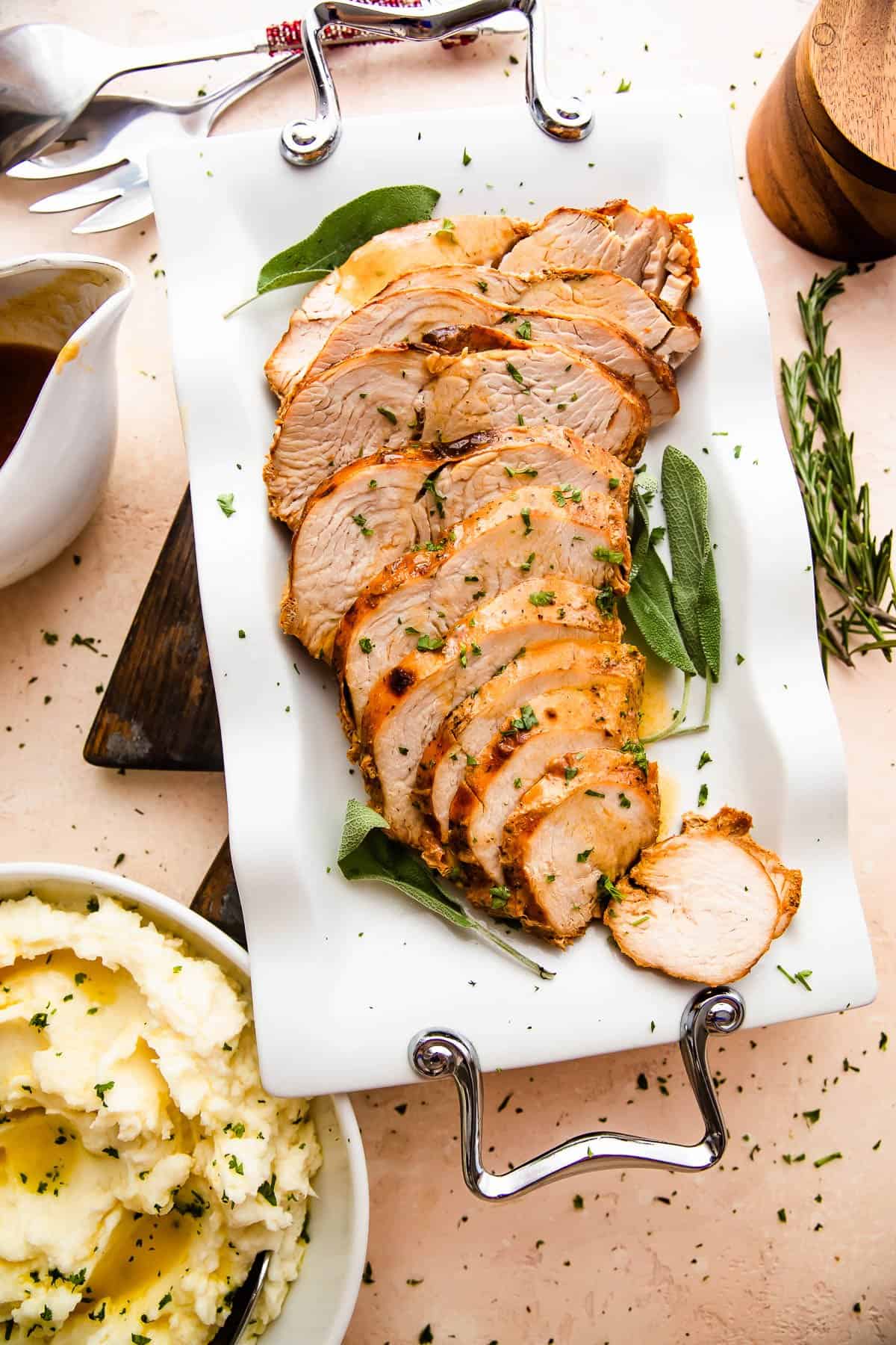wide view of sliced air fryer turkey breast arranged on a white platter with sage leaves placed on the sides of the turkey breast