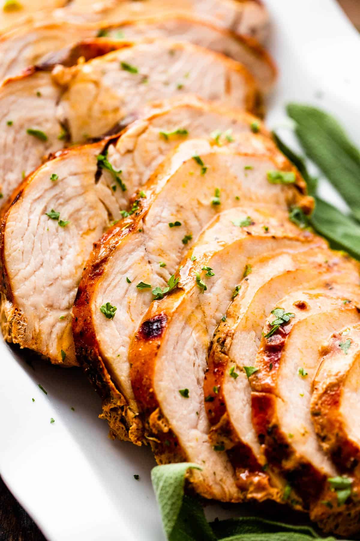 Sliced air fryer turkey breast drizzled with gravy and arranged on a white platter with sage leaves placed on the sides of the turkey breast.