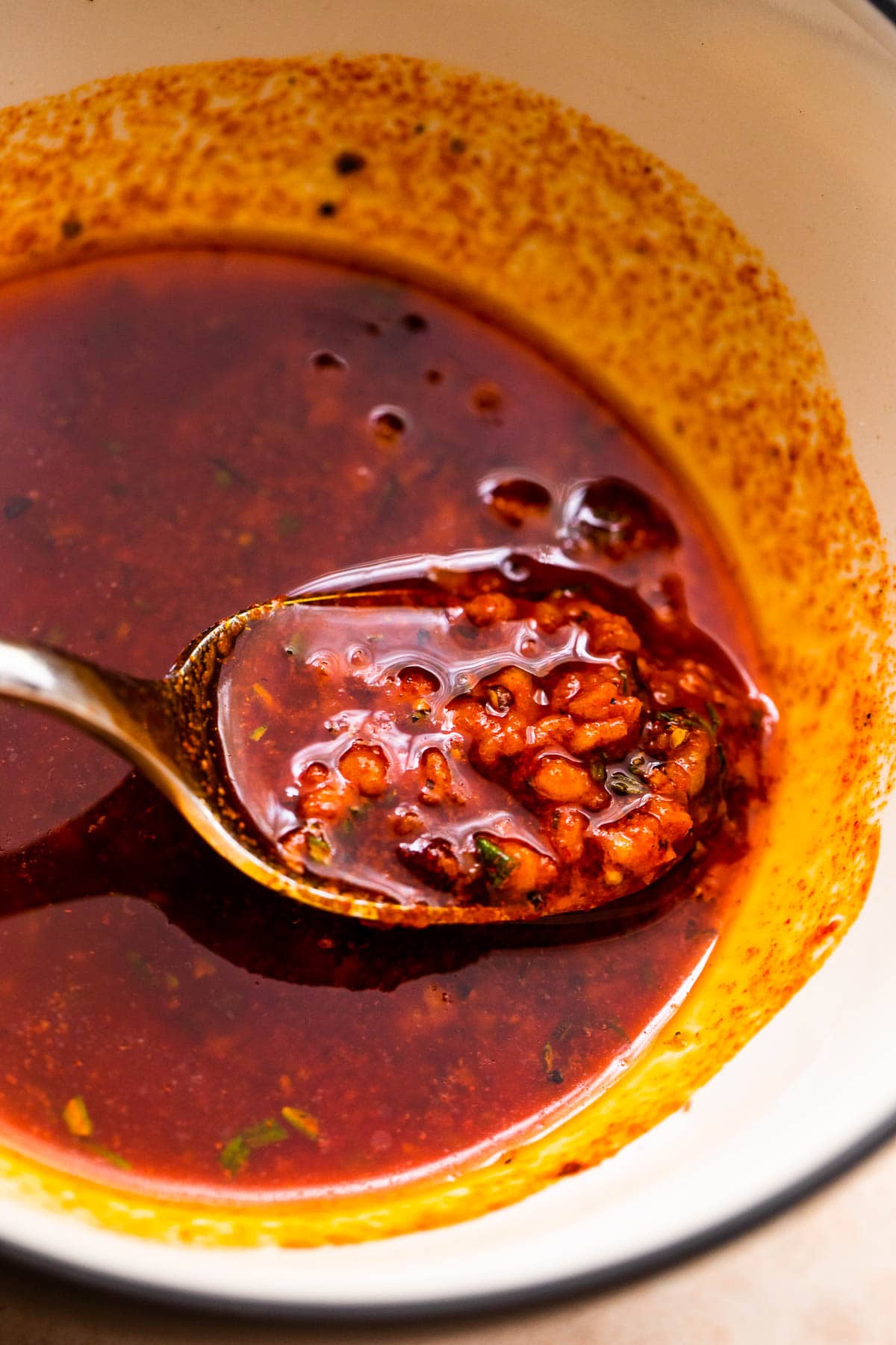 A spoon stirring through a mixture of cooking oil with garlic and paprika.