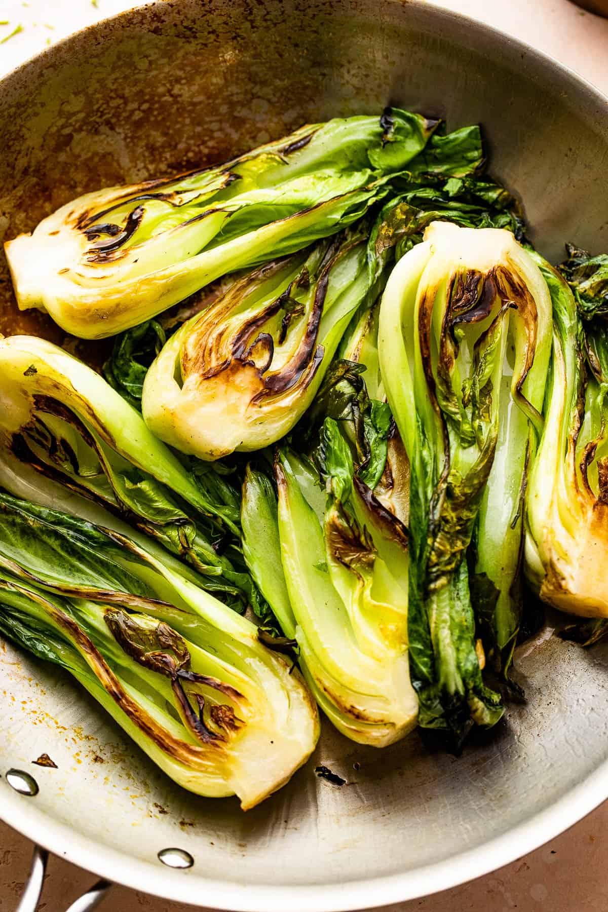 frying halved baby bok choy in a stainless steel skillet.